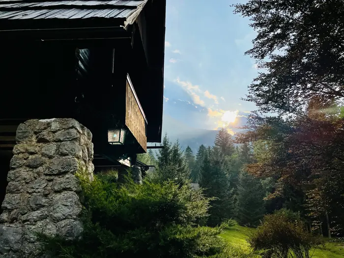 Kamniti steber in kovana svetilka Koče pri Rdeči Bukvi ob mraku, v ozadju gozd in večerno nebo